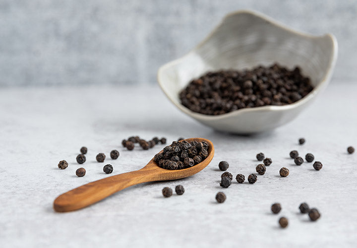 Black Kampot peppercorns in a ceramic dish and wooden spoon.